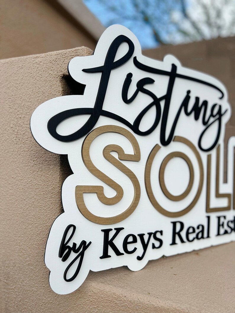 May include: White sign with black lettering that reads "Listing Sold by Keys Real Estate". The word "Sold" is in gold lettering with a white outline.