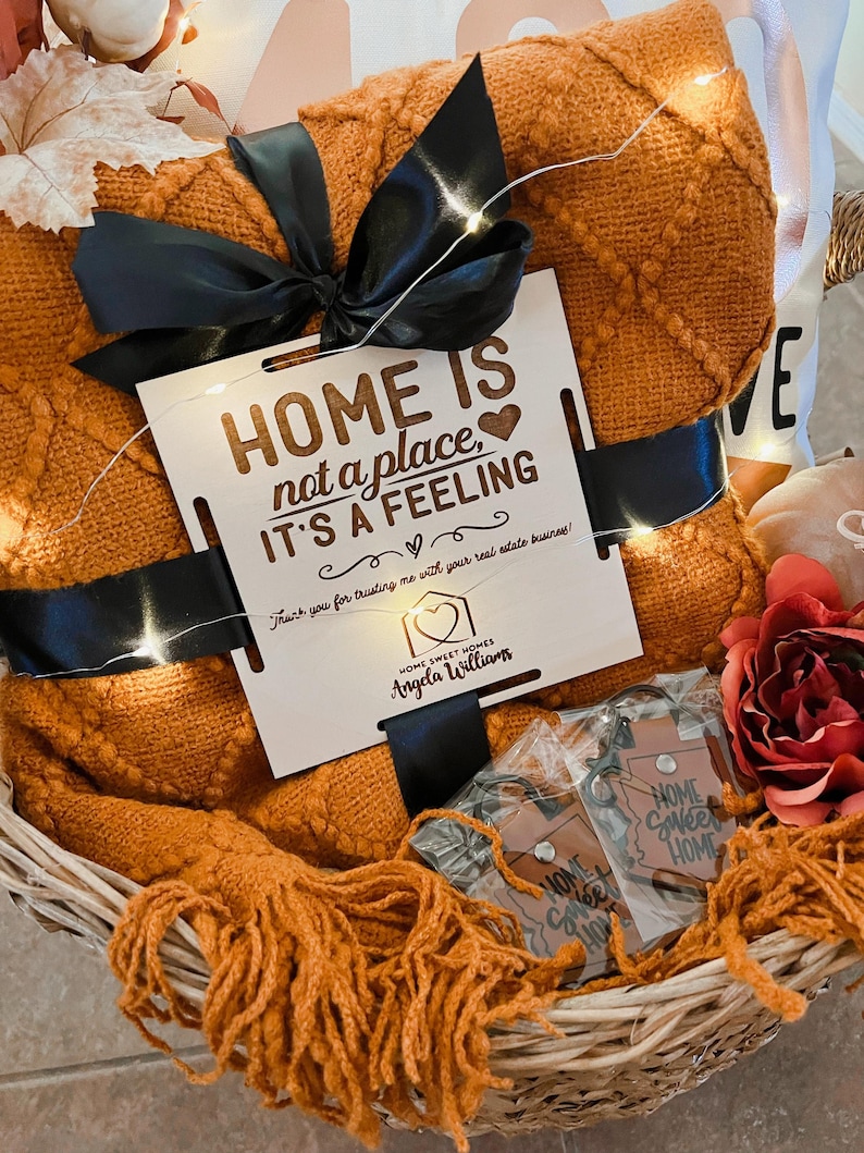 May include: A wicker basket filled with a cozy orange throw blanket, a wooden sign that reads "HOME IS not a place, IT'S A FEELING", and a small house-shaped keychain with the text "HOME SWEET HOMES Angela Williams".