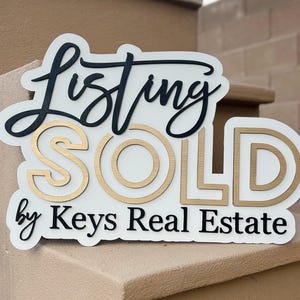May include: White sign with black and gold lettering that reads "Listing SOLD by Keys Real Estate".
