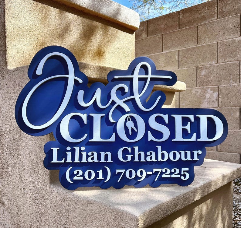 Pu&ograve; includere: Un'insegna personalizzata blu scuro e bianca con il testo "Just CLOSED", un'icona a forma di chiave che sostituisce la lettera O, seguita dal nome "Lilian Ghabour" e dal numero di telefono "(201) 709-7225" in un design audace, stratificato e 3D.