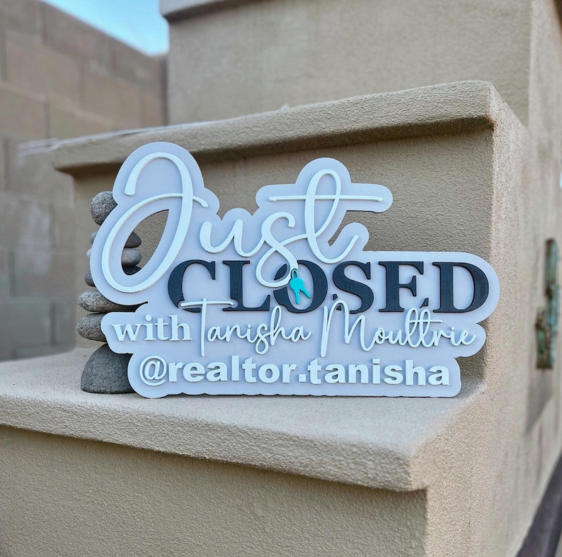 Pu&ograve; includere: Un'insegna 3D a strati con il testo Just CLOSED with Tanisha Moultrie e @realtor.tanisha. L'insegna presenta uno sfondo grigio chiaro con scritte grigio scuro e una piccola icona a forma di chiave color turchese integrata nella parola Just.
