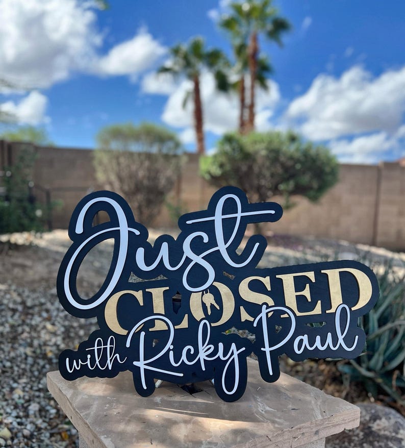 Pu&ograve; includere: Un cartello nero e oro con scritte bianche e dorate che recita Just CLOSED with Ricky Paul. Il cartello presenta una sagoma di una chiave di casa integrata nella parola CLOSED ed &egrave; progettato con una combinazione di caratteri corsivi e stampatello.