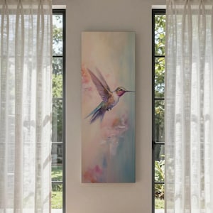 May include: A tall, rectangular wall art piece featuring a painting of a hummingbird in flight. The bird displays iridescent green, blue, and pink plumage against a soft, abstract background of blended pastel colors including peach, cream, and light blue.