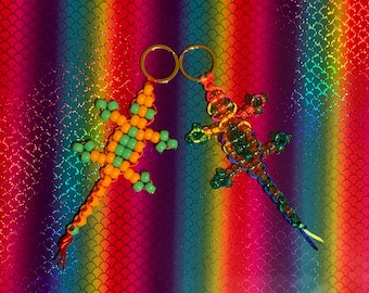 May include: Two beaded lizard keychains, one green and orange, the other green, orange, and blue, on a rainbow background.
