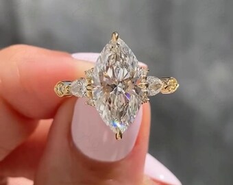 May include: A marquise-cut diamond ring with a gold band. The ring features a large, clear marquise-cut diamond as the centerpiece, flanked by smaller pear-shaped diamonds. The band has intricate detailing.