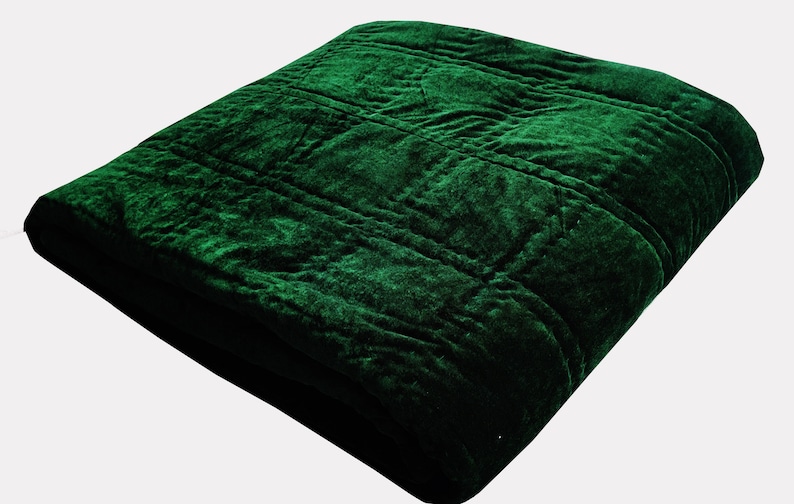 Puede incluir: Una manta de terciopelo verde oscuro con un patr&oacute;n acolchado.