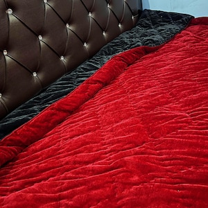 May include: A bed with a brown leather headboard with diamond tufting and crystal accents. A black velvet blanket and a red velvet blanket are on the bed, creating a layered look. The blankets add texture and color to the bedroom.