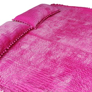May include: A bright pink bedspread with two matching pillows. The bedspread and pillows have a textured, quilted appearance and are trimmed with small pink pom-poms. The set is designed for a bed or lounging area.