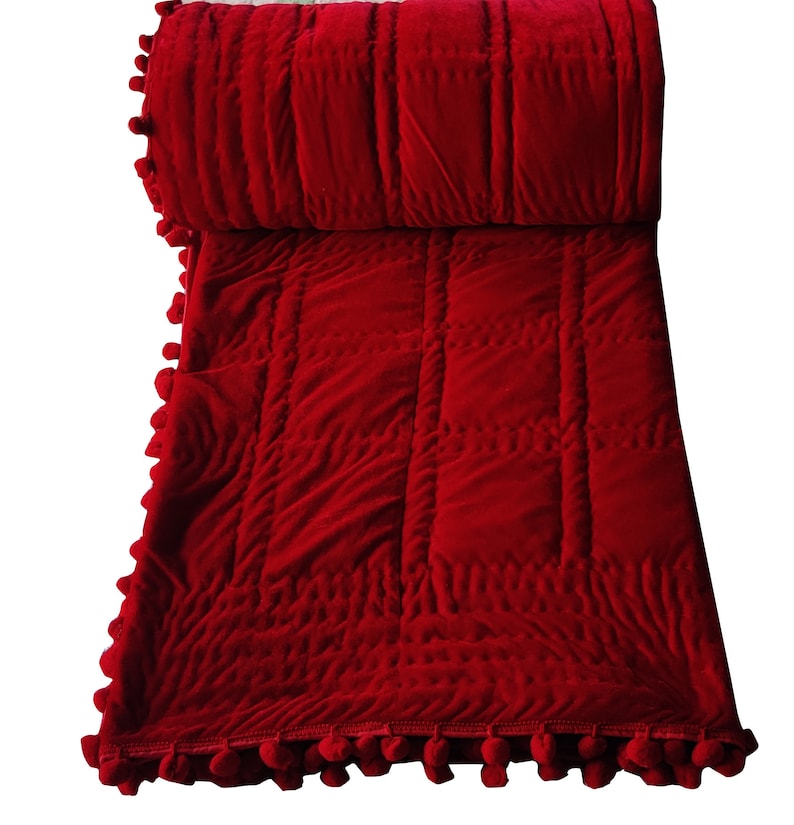 Puede incluir: Manta de tiro acolchada de terciopelo rojo con ribete de pompones. La manta est&aacute; doblada por la mitad y los pompones son visibles en ambos lados.
