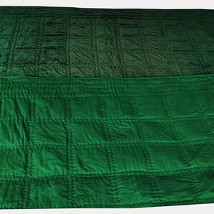 Puede incluir: Una manta acolchada verde con un patr&oacute;n degradado. La manta est&aacute; doblada por la mitad y la mitad superior es de un tono de verde m&aacute;s oscuro que la mitad inferior.