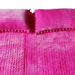 May include: A vibrant pink bedspread and two matching pillows. The bedspread and pillows feature a quilted design. The rectangular pillows are trimmed with small pink pom-poms. The bedding is a solid, bright colour.