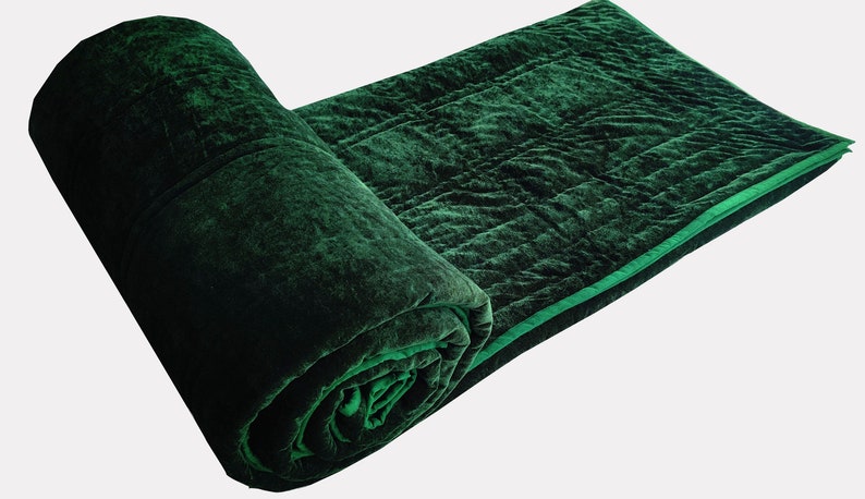 Puede incluir: Una manta de tiro acolchada de terciopelo verde oscuro con un borde verde claro. La manta est&aacute; enrollada y el extremo est&aacute; metido debajo de la manta.