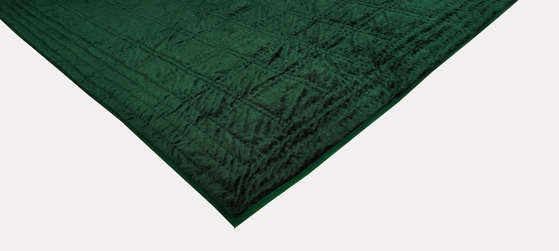 Puede incluir: Una manta de felpa verde oscuro acolchada con una superficie texturizada.