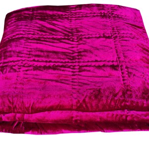 K&ouml;nnte beinhalten: Eine gefaltete rosa Samtdecke mit gestepptem Muster.