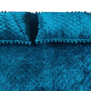 May include: A teal bedspread set with two matching pillows. The bedspread and pillows feature a quilted diamond pattern and are trimmed with small, matching pom-poms. The fabric has a crushed velvet texture.