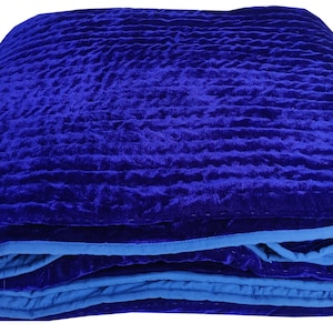 K&ouml;nnte beinhalten: Eine gefaltete blaue Samtdecke mit blauem Saum. Die Decke hat ein gestepptes Muster und ist aus einem weichen, luxuri&ouml;sen Stoff gefertigt.