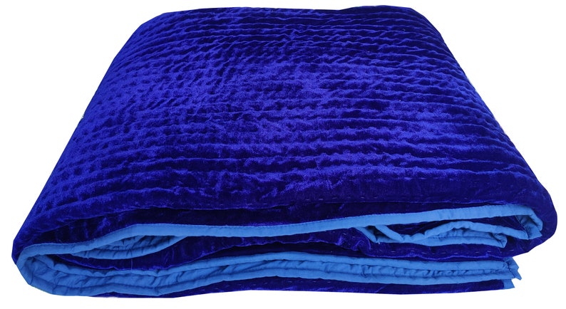 K&ouml;nnte beinhalten: Eine gefaltete blaue Samtdecke mit blauem Saum. Die Decke hat ein gestepptes Muster und ist aus einem weichen, luxuri&ouml;sen Stoff gefertigt.