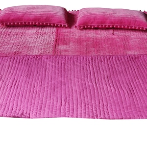 May include: A bright pink bedspread set with two matching pillows. The bedspread has a textured, quilted design and a solid pink border. The pillows are decorated with small pink pom-poms along the edges, adding a decorative touch to the bedding.