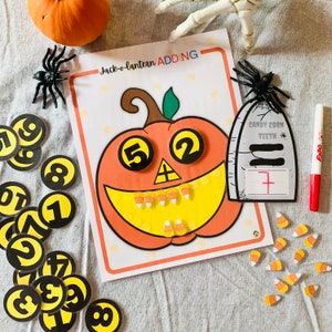 Könnte beinhalten: Eine druckbare Halloween-Mathe-Aktivität mit einer Kürbislaterne mit Mais-Zähnen. Die Zahlen 5 und 2 befinden sich auf den Augen der Kürbislaterne. Der Text "Jack-o-lantern ADDING" befindet sich oben auf der Seite. Ein Grabstein mit dem Text "Candy Corn Teeth" befindet sich auf der rechten Seite der Seite.