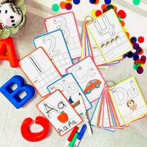 May include: A set of colorful flashcards with uppercase letters and numbers for kids to learn the alphabet and numbers. The cards are laid out on a white and gray striped surface with colorful counters and markers.
