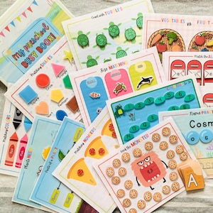 Może przedstawiać: Zbiór kolorowych zajęć edukacyjnych dla przedszkolaków. Zawiera książeczkę, karty do dopasowywania kształtów i kolorów, gry rozpoznawania liczb i liter oraz grę w sortowanie warzyw i owoców. Materiały zawierają ilustracje żółwi, pizzy i potworów.