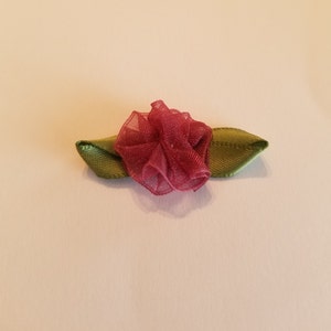 May include: A handmade fabric flower with a ruffled, burgundy center and two green satin leaves. The flower is likely used for crafting, scrapbooking, or as an embellishment for clothing or accessories. The flower is approximately 2 inches wide.