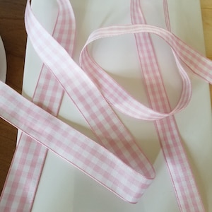 May include: Pink and white gingham ribbon, ideal for crafts and gift wrapping. The ribbon is made of a smooth, woven material and features a classic checkered pattern. The ribbon is approximately 0.5 inches wide.