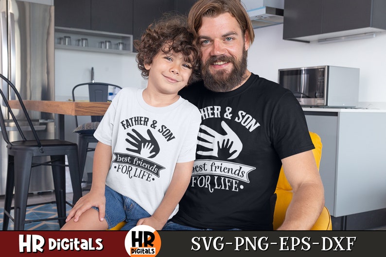 Op de afbeelding: Een wit T-shirt met de tekst "Father & Son best friends for life" en een zwart T-shirt met de tekst "Father & Son best friends for life". Beide shirts hebben een handafdruk-ontwerp.