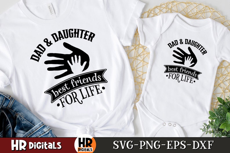 Op de afbeelding: Twee witte T-shirts met zwarte tekst en afbeeldingen. Het grotere shirt zegt "Papa & Dochter beste vrienden voor het leven" met een afbeelding van twee handen, een grote en een kleine, die elkaar aanraken. Het kleinere shirt zegt "Papa & Dochter beste vrienden voor het leven" met dezelfde handafbeelding.