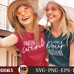 Puede incluir: Dos mujeres con sombreros de paja y gafas de sol sonr&iacute;en y se toman una selfie. Una mujer lleva una camiseta roja con el texto "Partners in wine" y la otra lleva una camiseta azul con el texto "Expert in pour decisions".