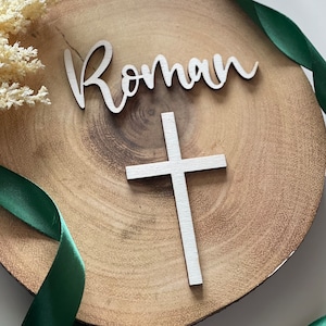 May include: A wooden plaque with the name "Roman" written in cursive and a white wooden cross.