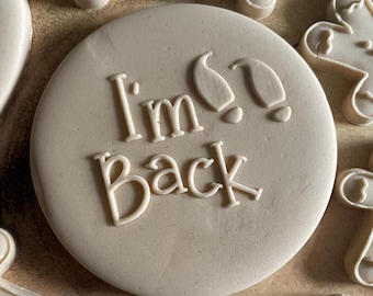 Op de afbeelding: Een ronde, beige koek met de tekst "I'm Back" en twee voetafdrukken in witte glazuur.