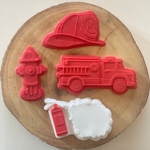 May include: Four red silicone cookie cutters shaped like a fire hydrant, a fire engine, a fire hat, and a fire extinguisher with a white cloud of smoke.