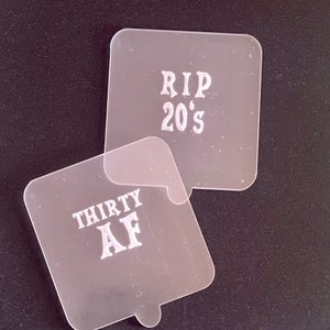 May include: Two clear plastic stencils with white lettering. The top stencil says "RIP 20's" and the bottom stencil says "THIRTY AF".