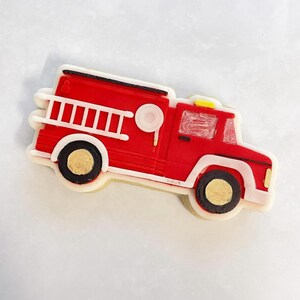 May include: Red and white fire engine cookie decorated with gold accents.