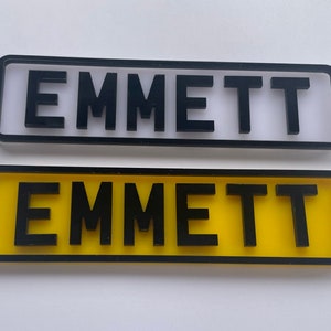 May include: Two personalised nameplates with the name "EMMETT" in black lettering. The top nameplate is white with a black border. The bottom nameplate is yellow with a black border.