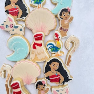 May include: A selection of decorated sugar cookies, each depicting characters and symbols from a well-known animated film. The cookies showcase a woman, a pig, a rooster, a baby, a seashell, and a wave, all with intricate icing details.