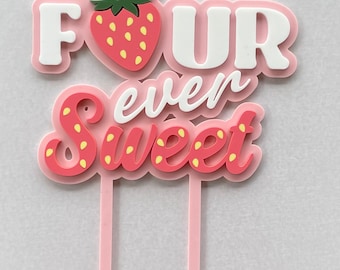 Puede incluir: Topper de pastel rosa y blanco con las palabras "FOUR even sweet" y una fresa roja con semillas amarillas. El topper tiene dos palitos rosas.