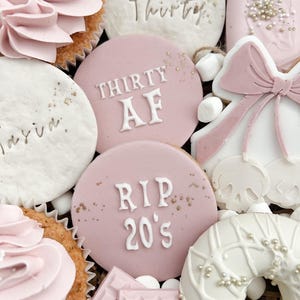 May include: A pink and white birthday gift box with cupcakes, cookies, and a donut. The cookies have the text "Thirty AF" and "RIP 20's" on them.