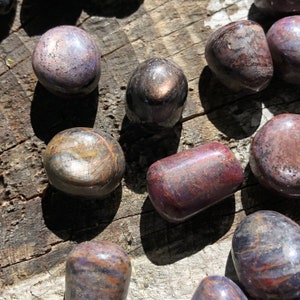 May include: A collection of tumbled stones in shades of purple, brown, and gold. The stones are smooth and polished, with a natural, organic look.