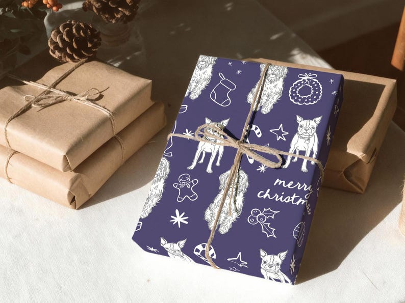 May include: A rectangular gift wrapped in dark purple paper featuring a white line art pattern of dogs, gingerbread men, stockings, wreaths, and holly, tied with brown twine. The text "merry christmas" is printed in white on the paper.