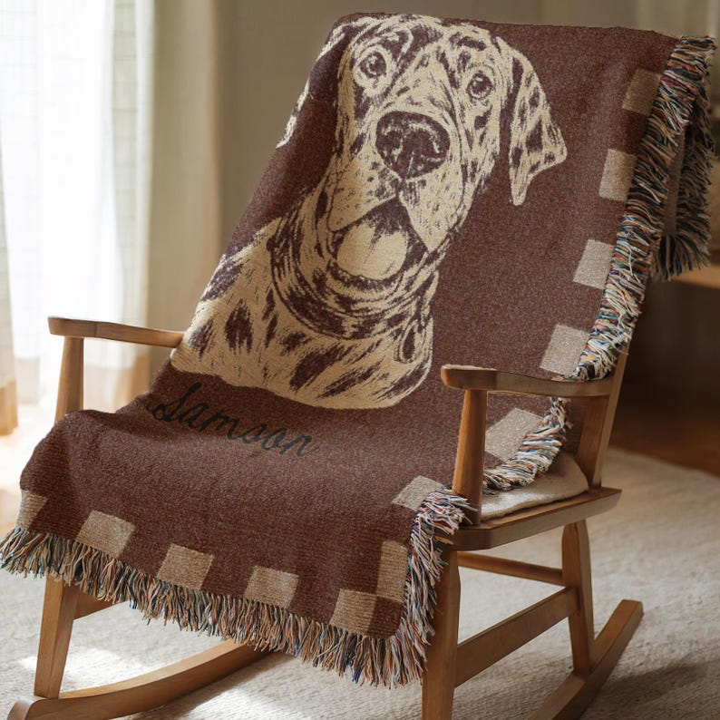 May include: A brown throw blanket draped over a wooden rocking chair. The blanket features a large dog portrait in beige and brown, with the name "Samson" in script. The blanket has a checkered border and fringed edges.