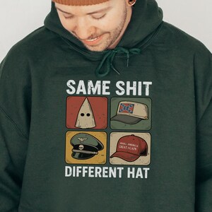 Könnte beinhalten: Waldgrüner Kapuzenpullover mit dem Text "SAME SHIT DIFFERENT HAT" und vier Bildern von verschiedenen Hüten. Der Hoodie hat auch eine braune Mütze. Der Text "FOREST GREEN" befindet sich unten rechts.