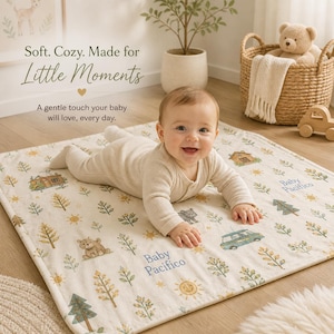 May include: A baby lies on a cream-colored blanket with a pattern of trees, suns, houses, and bears. The blanket has the text "Baby Pacifico" in blue. The baby is wearing a light-colored onesie and smiling. The text "Soft. Cozy. Made for Little Moments" is at the top.