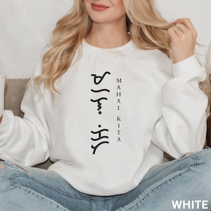 May include: A white long-sleeve crewneck sweatshirt featuring black text that reads "MAHAL KITA" vertically alongside a column of black Baybayin script characters. The garment has a standard fit with ribbed cuffs and a ribbed neckline.