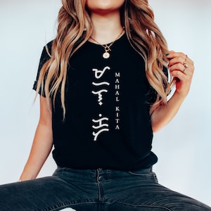 May include: A black short-sleeved t-shirt featuring white text printed vertically on the centre chest. The design includes Baybayin script characters stacked above the English words "MAHAL KITA" written in a clean, sans-serif white font.