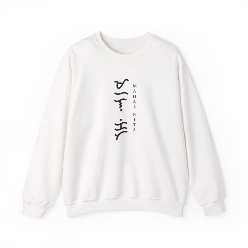 May include: A white long-sleeve crewneck sweatshirt featuring black text printed vertically on the centre chest. The design includes Baybayin script characters arranged in a column next to the words "MAHAL KITA" written in a simple serif font.