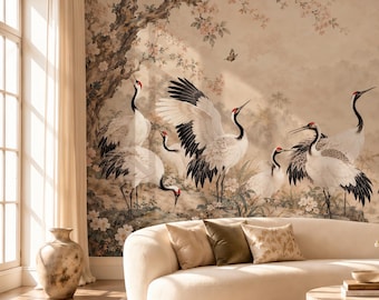 May include: A curved cream-colored sofa sits before a large wall mural featuring multiple white and black cranes in a landscape with trees and flowers. A round stone coffee table holds a vase with flowers and books, while a large vase stands nearby.
