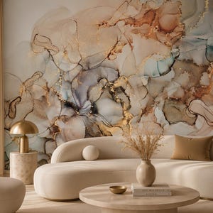 Pode incluir: Um sofá curvo de cor creme e uma poltrona a condizer estão dispostos numa sala com um grande mural de parede com redemoinhos abstratos de bege, castanho, azul e dourado. Uma mesa de centro redonda contém um vaso com erva seca.