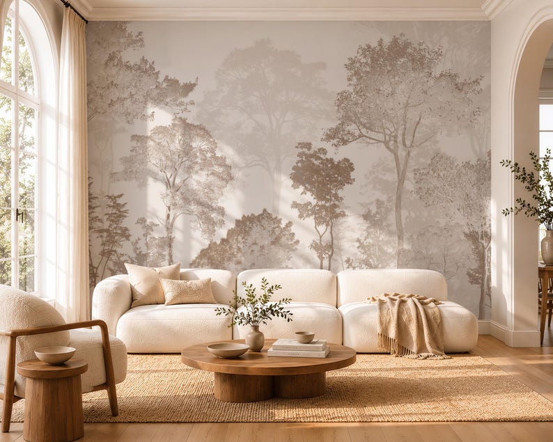 May include: A large-scale wall mural featuring a sepia-toned forest landscape with layered trees and foliage. The mural serves as a backdrop for a white modular sofa, a round wooden coffee table, and a matching armchair on a woven rug.